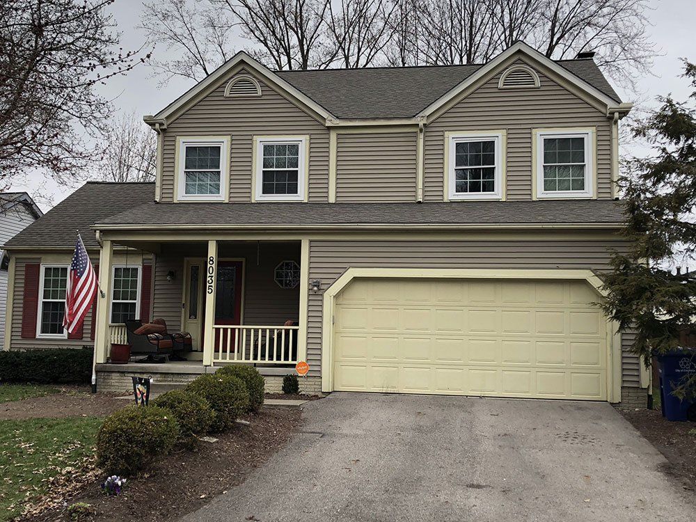 A large house with a yellow garage door and an american flag on the porch.