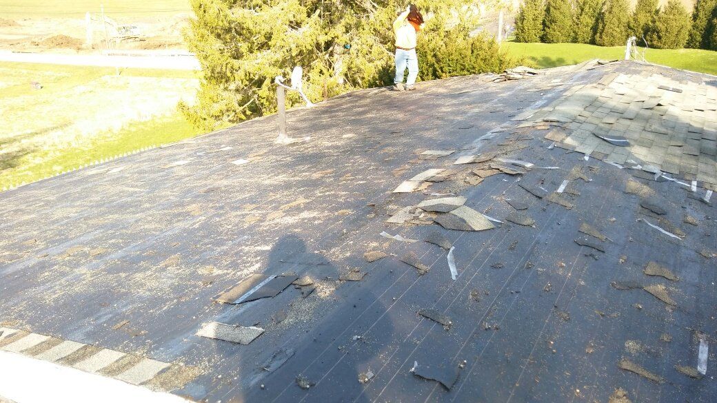 A person is standing on top of a roof that is covered in shingles.