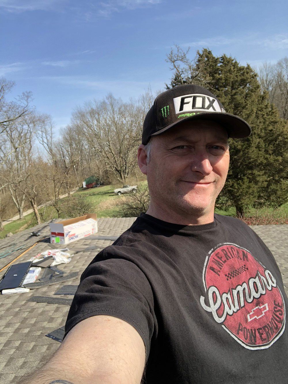 A man wearing a hat and a t-shirt is taking a selfie on a roof.