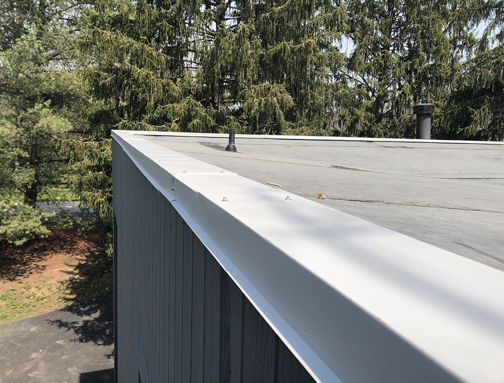 A roof with a gutter on it and trees in the background
