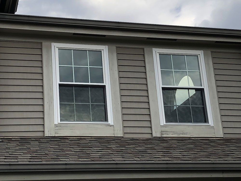 Two windows on the side of a house with a roof