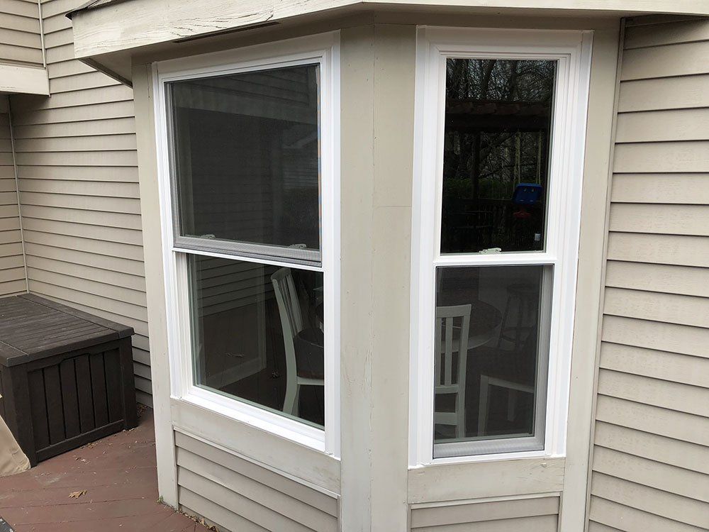 A bay window on the side of a house with a table and chairs.