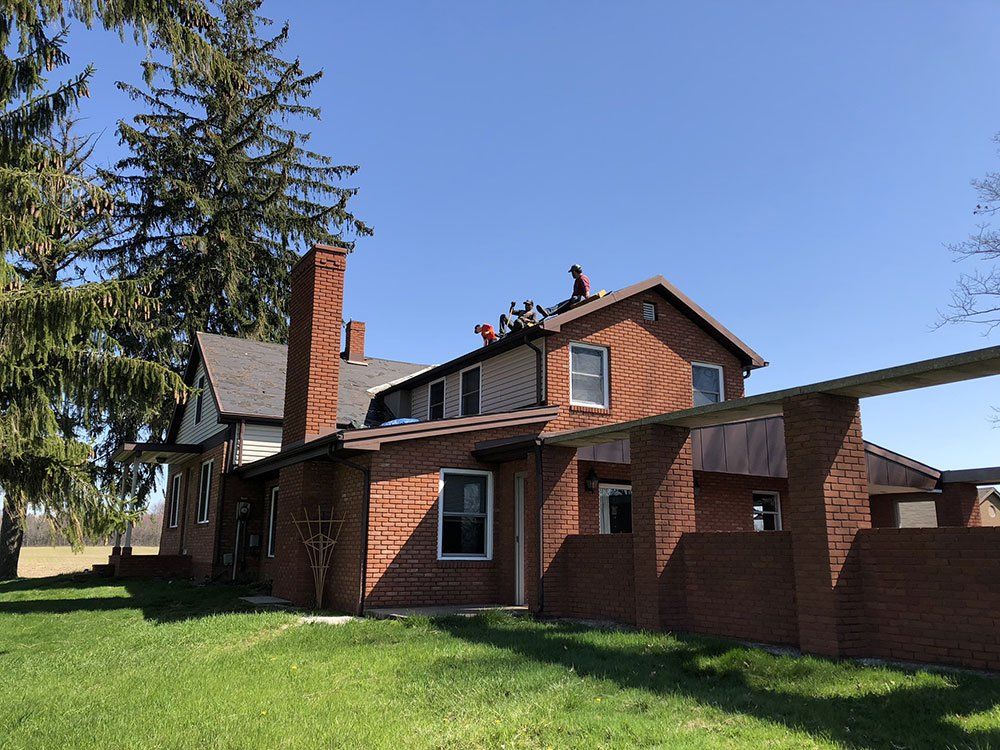 A man is standing on the roof of a brick house.