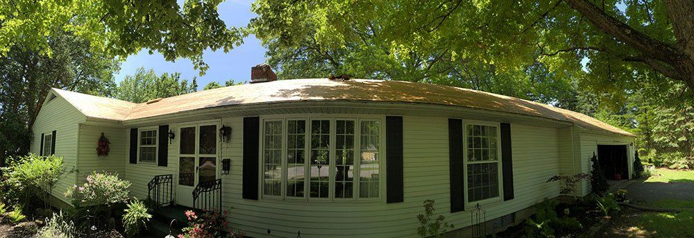 A white house with black shutters is surrounded by trees on a sunny day.
