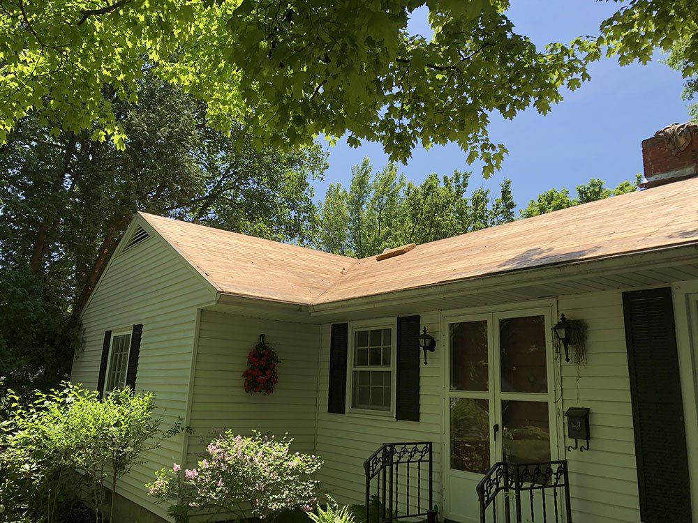 A white house with a brown roof and black shutters is surrounded by trees.