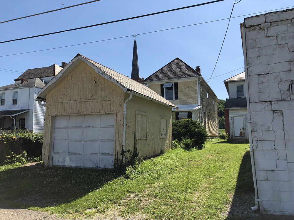 A garage with a white door is next to a house with a steeple in the background.