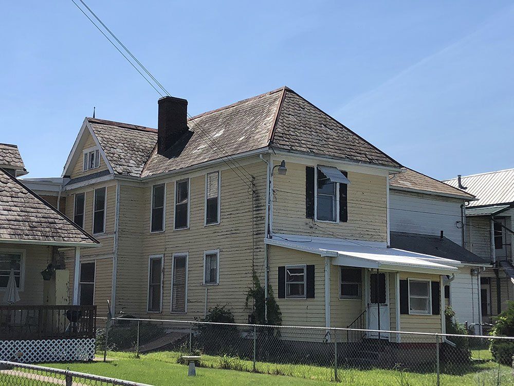 A large yellow house with a chimney on the roof is surrounded by a chain link fence.