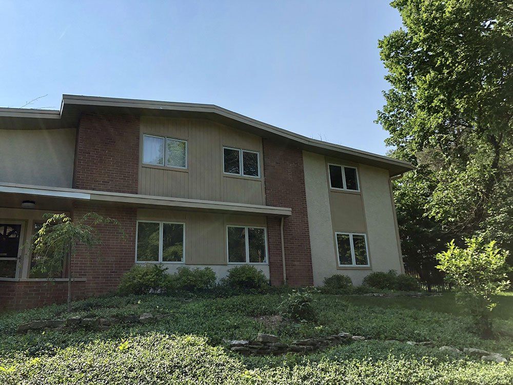 A large brick house with a lot of windows is sitting on top of a lush green hillside.