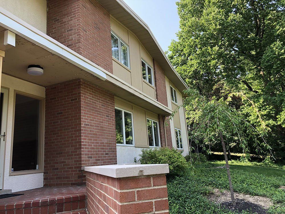 A brick house with a porch and a tree in front of it