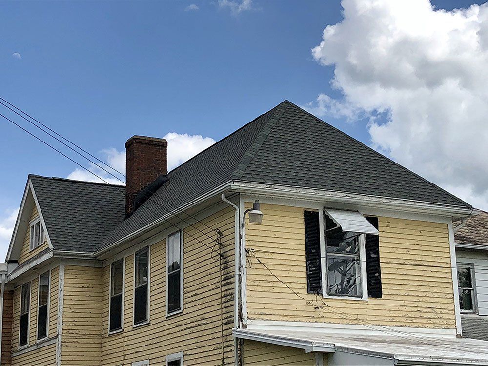 A yellow house with a black roof and black shutters.