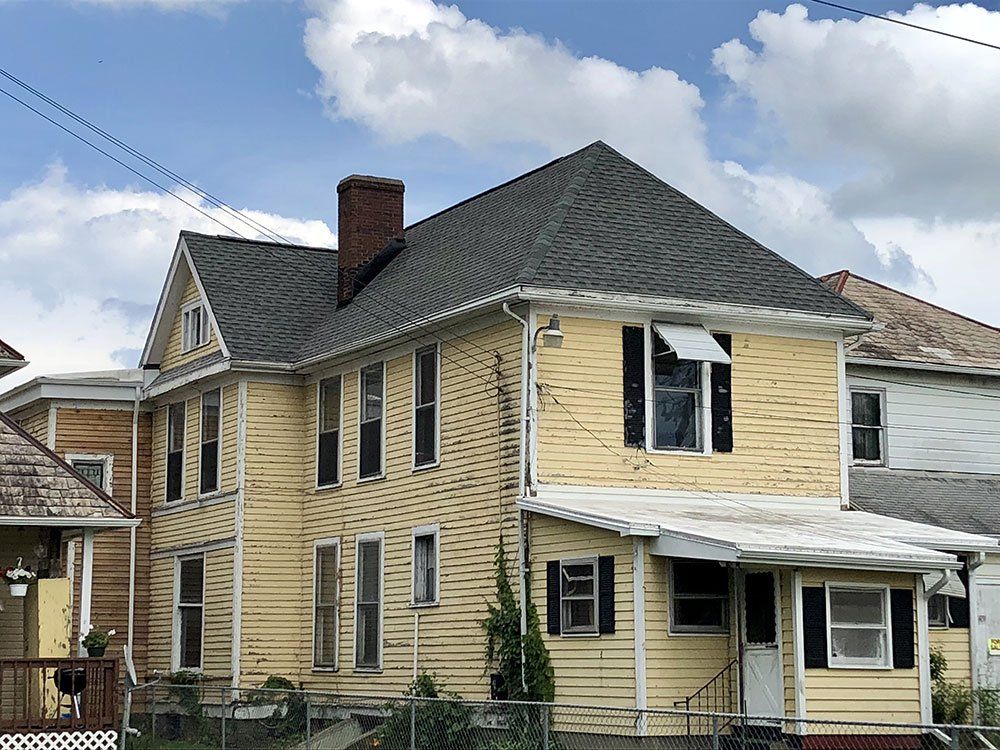 A large yellow house with a gray roof and black shutters.