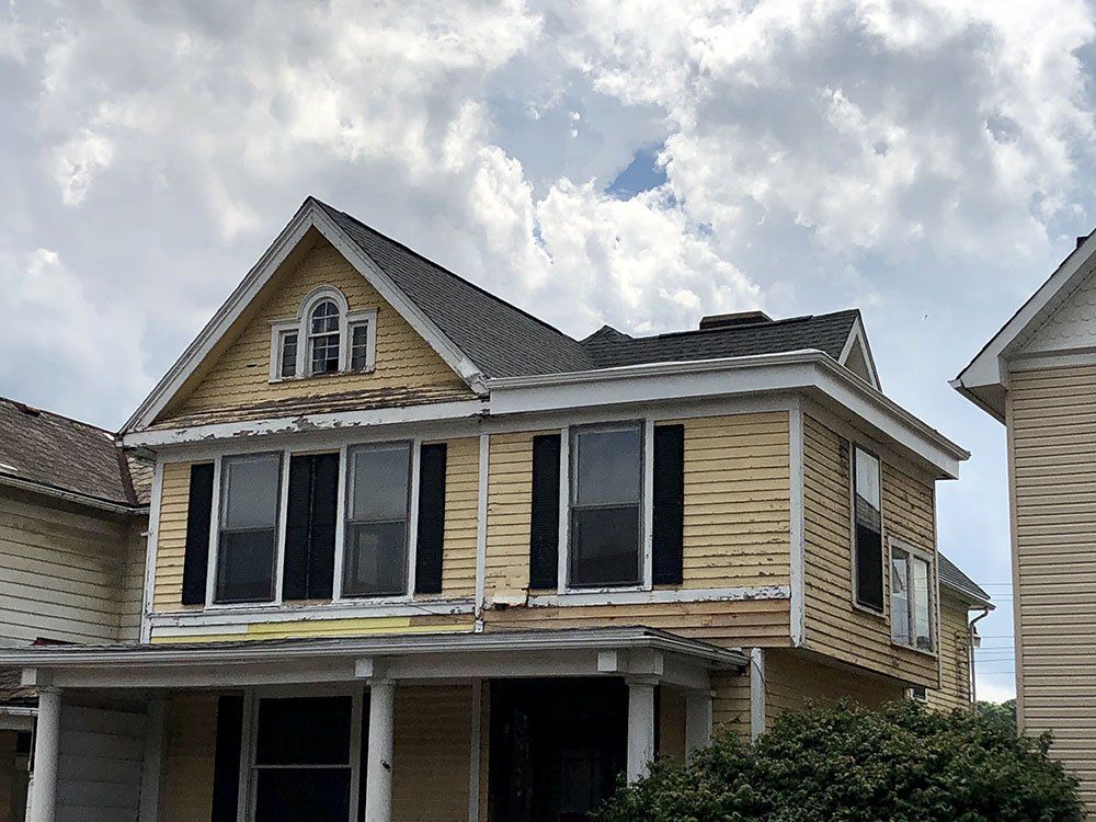 A yellow house with black shutters and a broken roof.