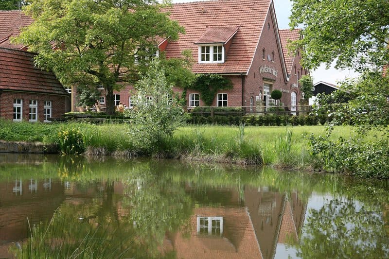 Ein Backsteinhaus spiegelt sich im Wasser eines Teichs.