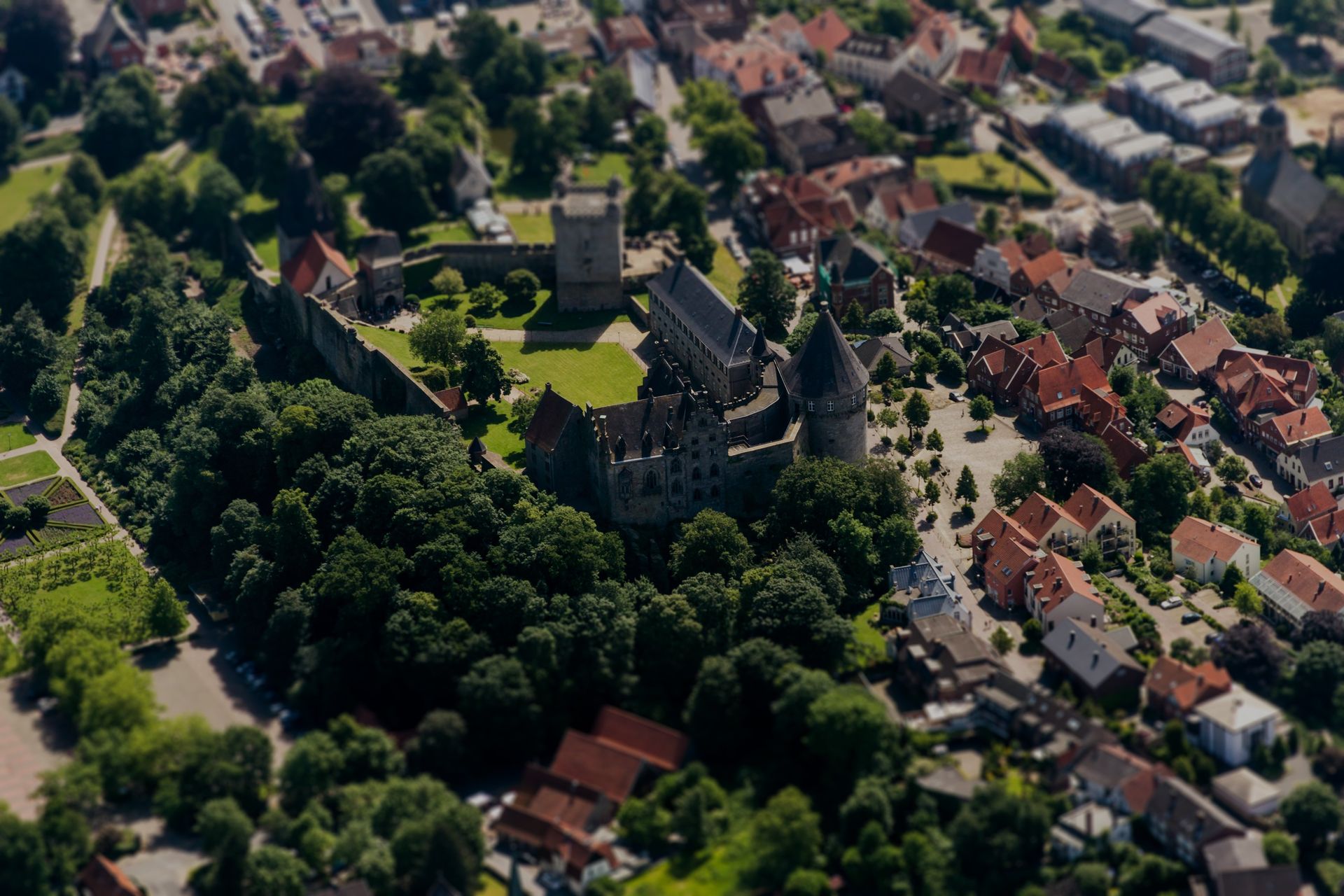 Een luchtfoto van een kasteel omgeven door bomen en huizen in een klein stadje.