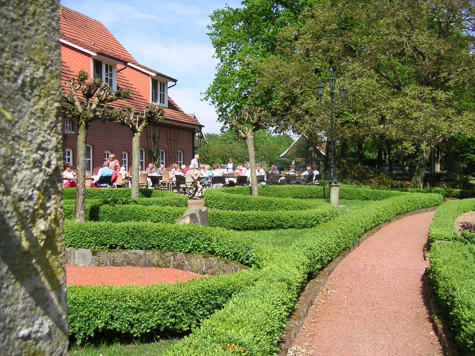 Eine Gruppe von Menschen sitzt an Tischen in einem Garten vor einem Backsteingebäude