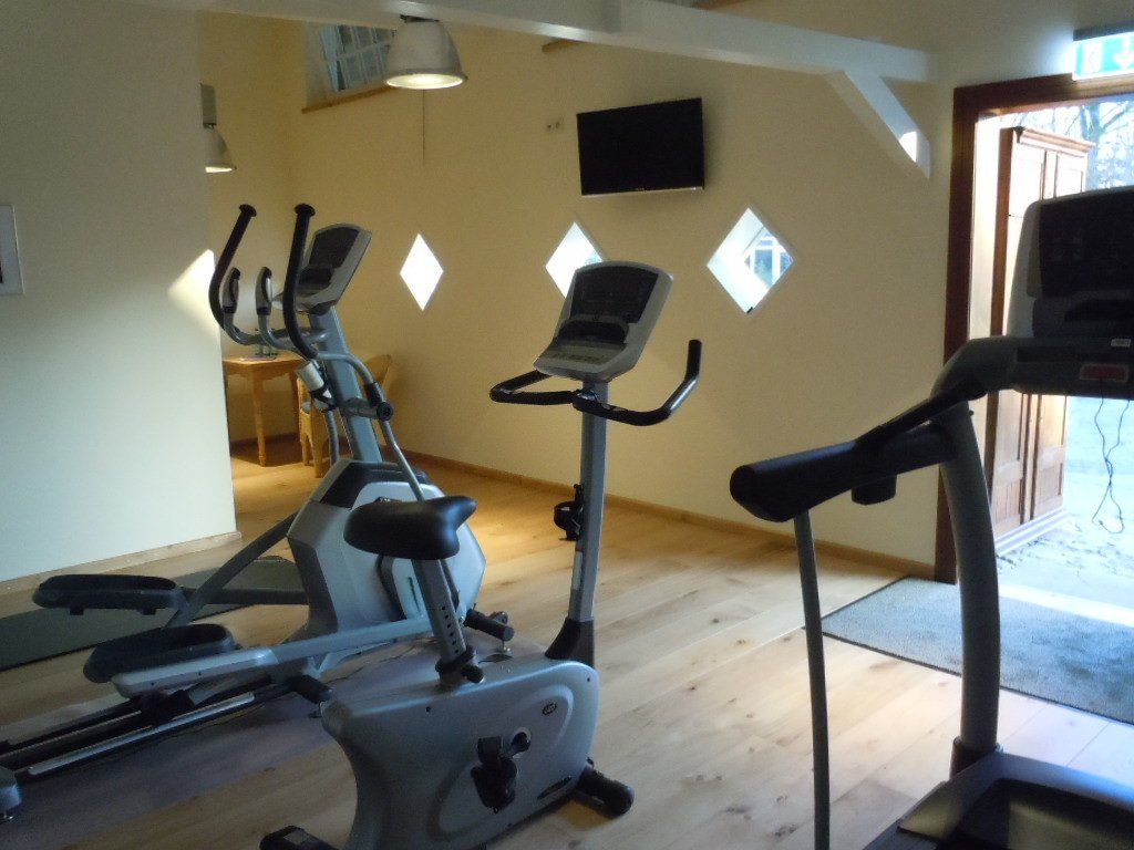 Een sportschool met een loopband, een fiets en een crosstrainer