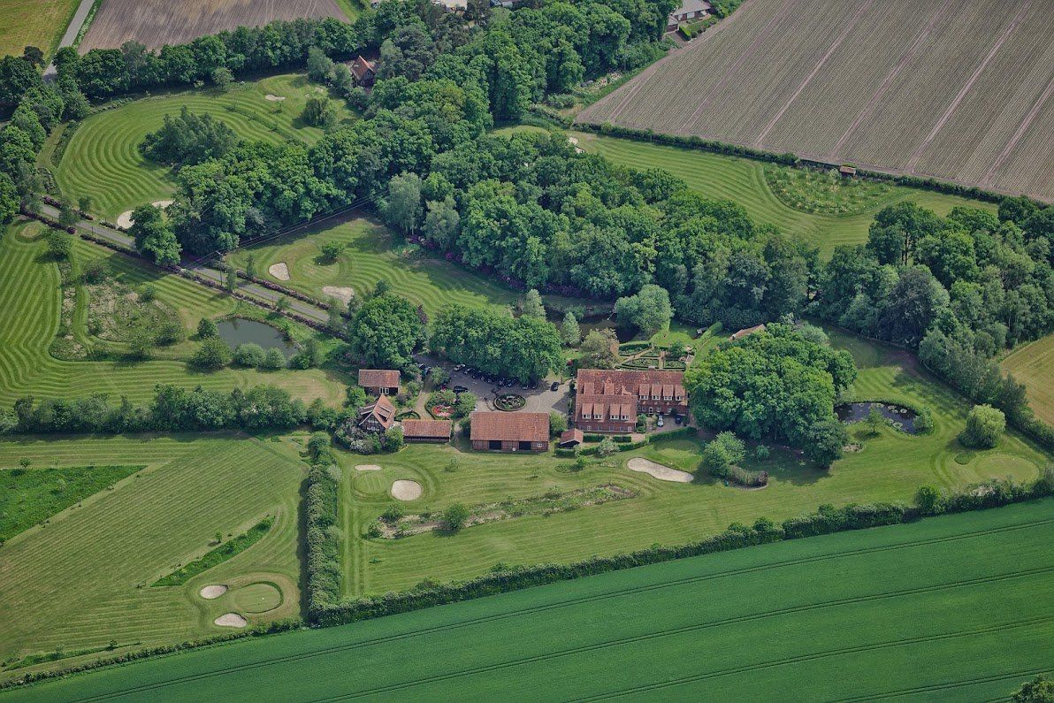 Een luchtfoto van een groot huis omgeven door velden en bomen.