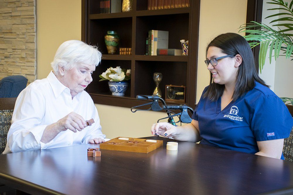 Woman playing game with healthcare worker at table. Shelves with items in background.