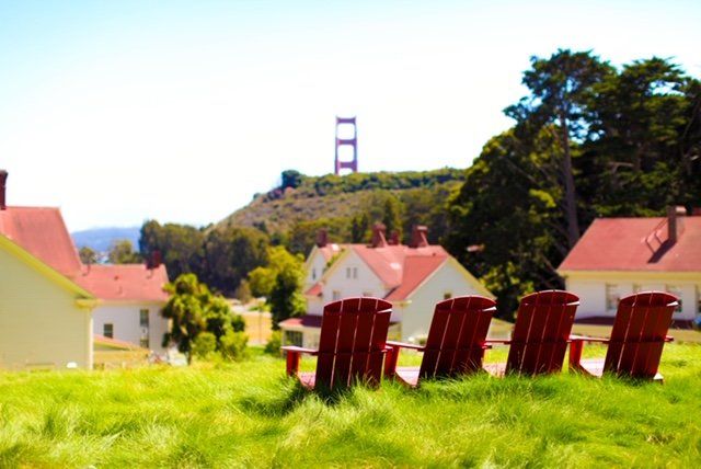 A row of red chairs in a grassy field with the golden gate bridge in the background