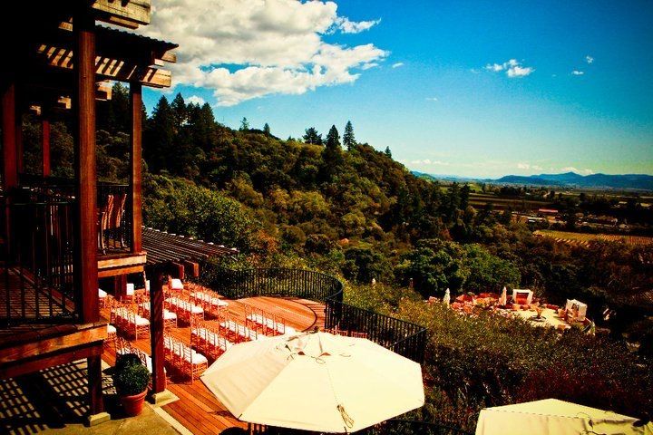 A row of tables and umbrellas on a deck overlooking a lush green hillside.
