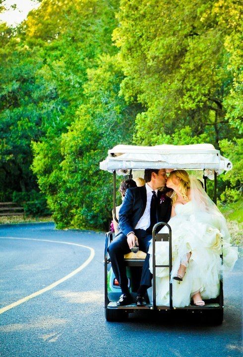 A bride and groom are kissing in a golf cart