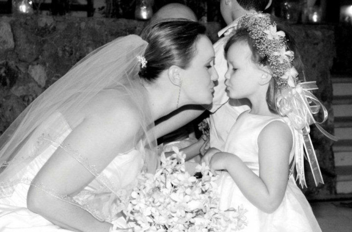 A bride is kissing her flower girl on the cheek.