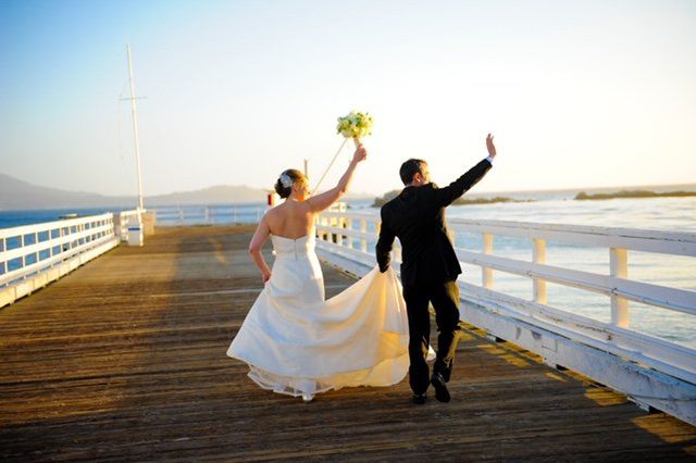 A bride and groom are walking on a pier.