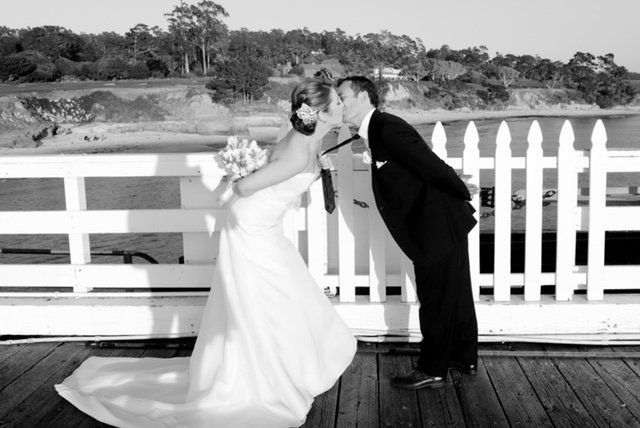 A bride and groom kissing on a pier in front of a white picket fence