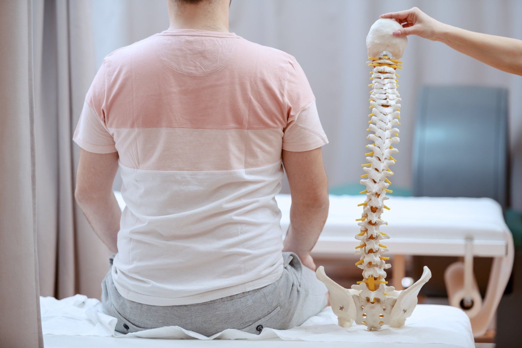 A man is sitting on a bed while a doctor examines his spine.
