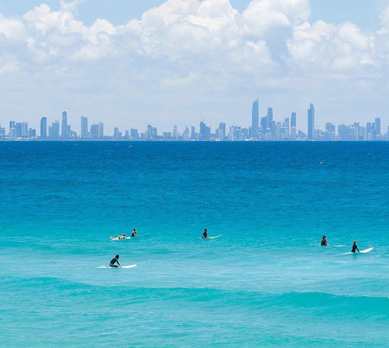 Surfers Sit on their Boards in front of the Surfer's Paradise Skyline — Safe N Sound Locksmiths in Varsity Lakes, QLD