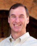 Smiling middle-aged man wearing a light-colored button-down shirt, outdoors.