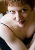 Woman with short red hair, smiling, looking up. Wearing a black spaghetti strap top.