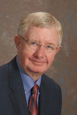 A man with glasses and a red tie, wearing a blue suit. He is smiling slightly.