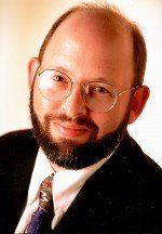A smiling man with a beard and glasses, wearing a suit and tie.