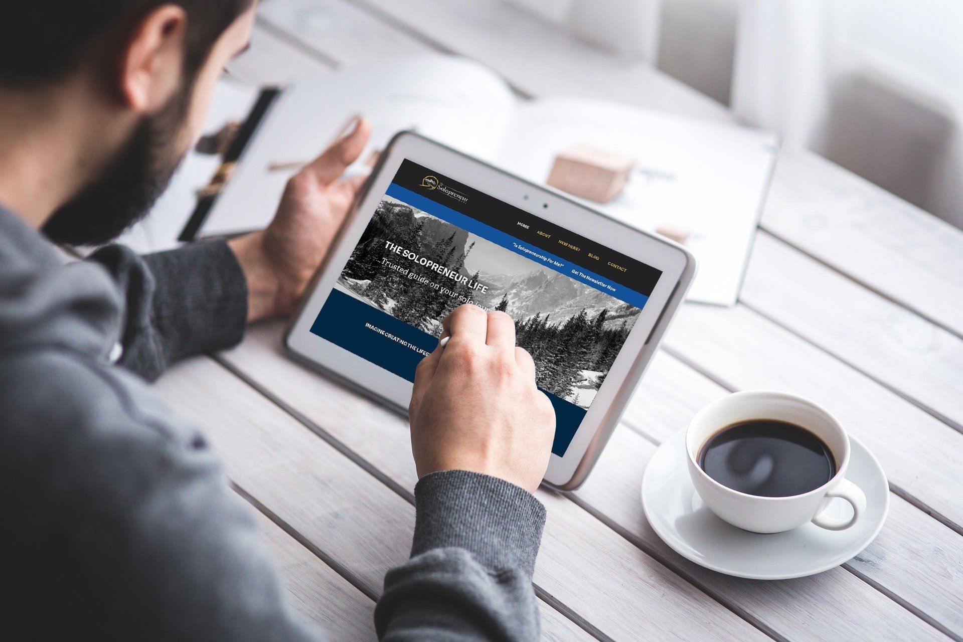 Person using a tablet on a table with a cup of coffee; website is open.
