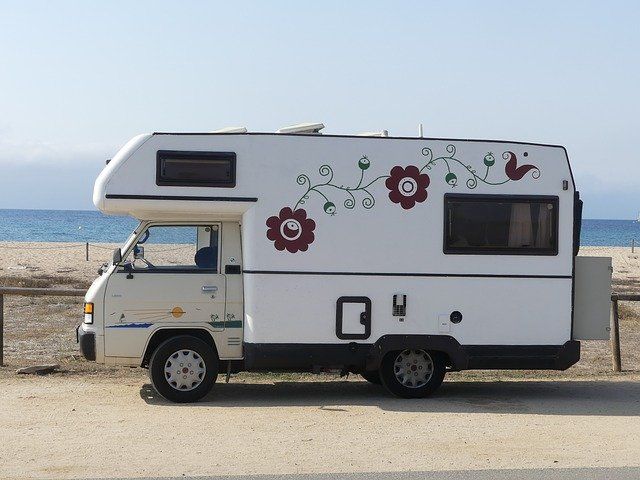 White campervan with floral decals parked on a road near a beach with blue water and sky.