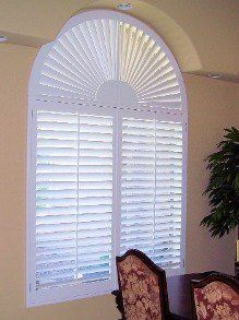 A dining room with a large window with arched shutters.