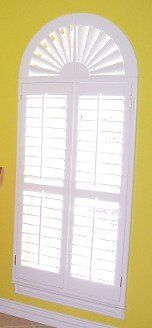A yellow wall with a white window with shutters on it.