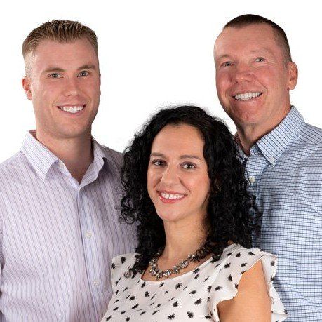 Three people smiling against a white background, wearing light-colored shirts and a polka-dot blouse.