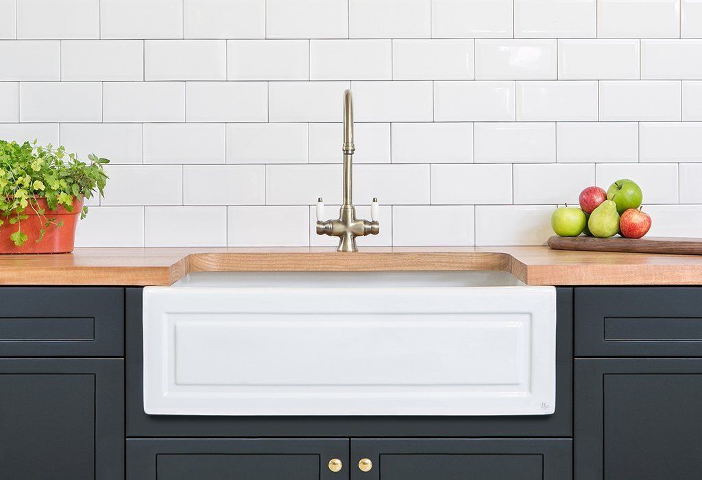 A farmhouse sink against timber bench top, navy cabinets and white subway tile. A farmhouse sink against timber bench top, navy cabinets and white subway tile.