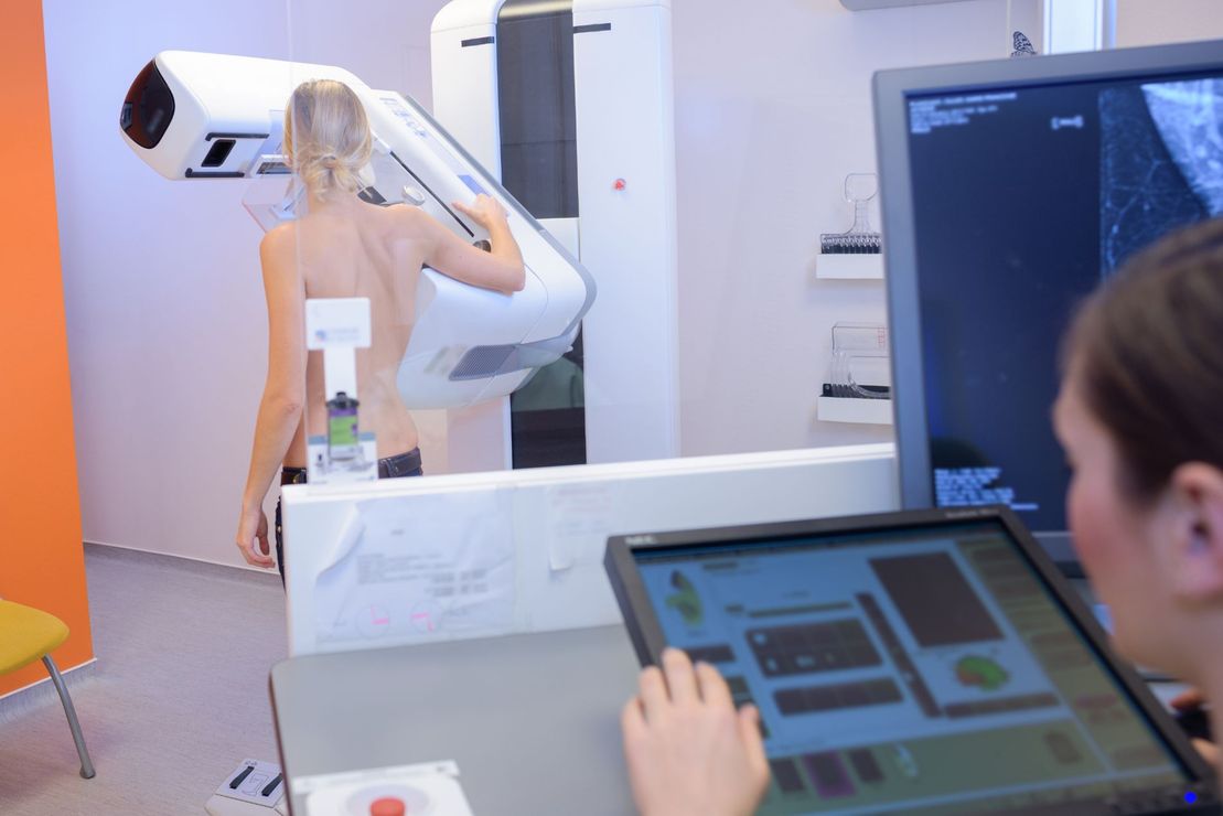 Una persona utilizza un tablet mentre una donna aziona uno scanner medico in un laboratorio luminoso.