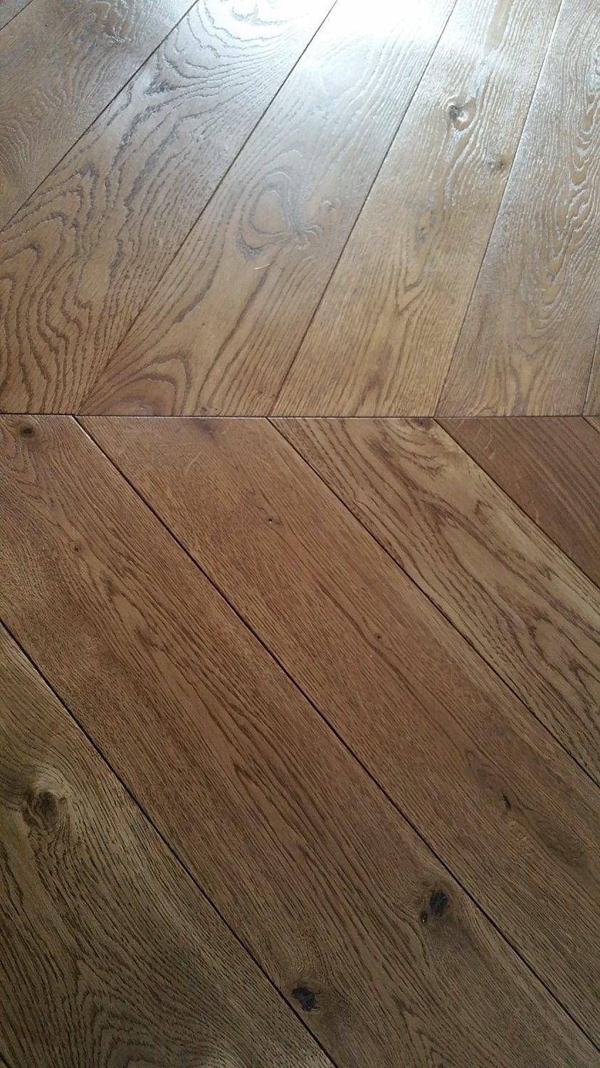 Pavimento in legno con motivo a chevron, con diverse tonalità di marrone e venature del legno visibili.