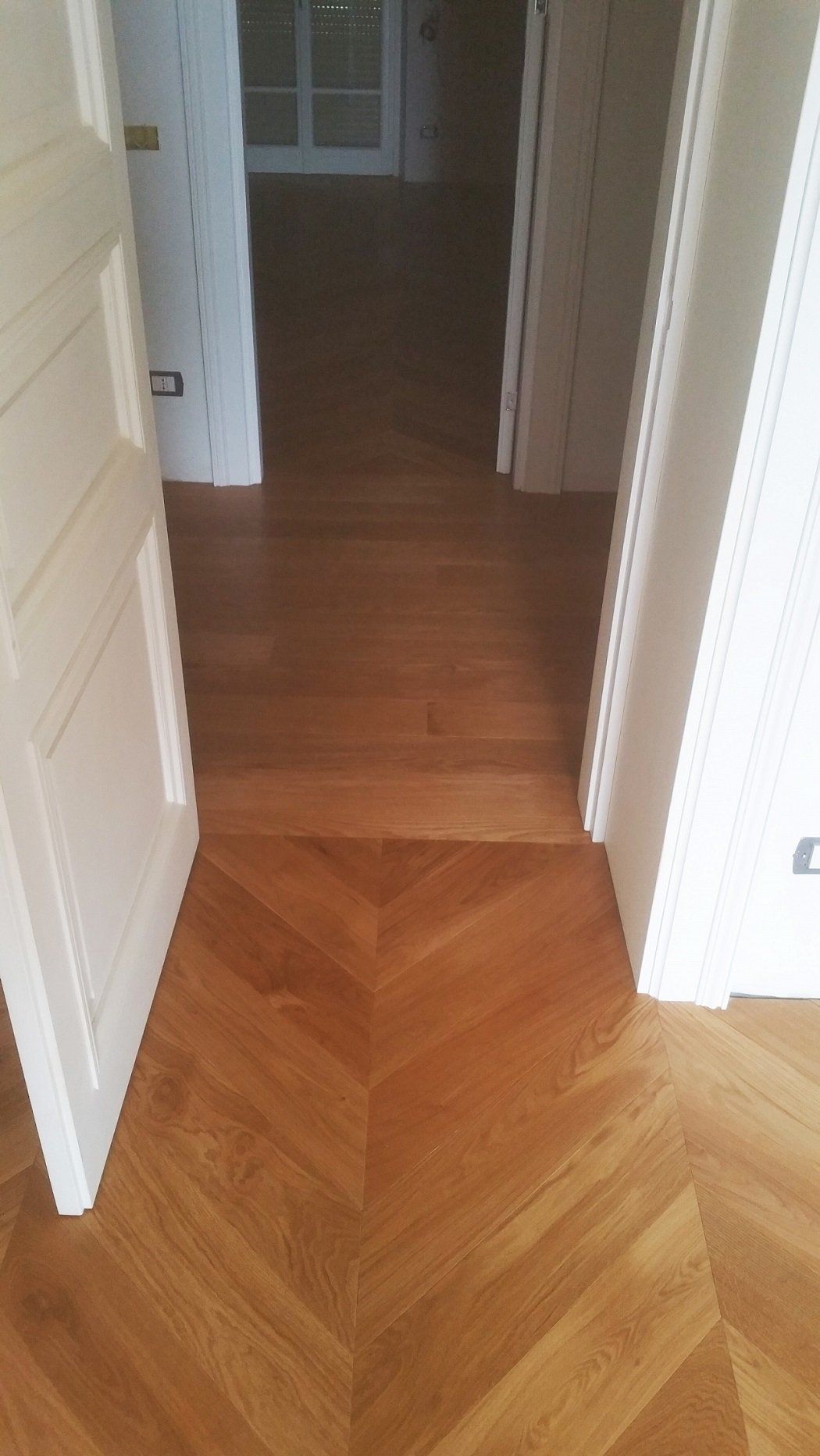 Un pavimento in legno a spina di pesce conduce, attraverso una porta aperta, in una stanza con pavimenti in legno.
