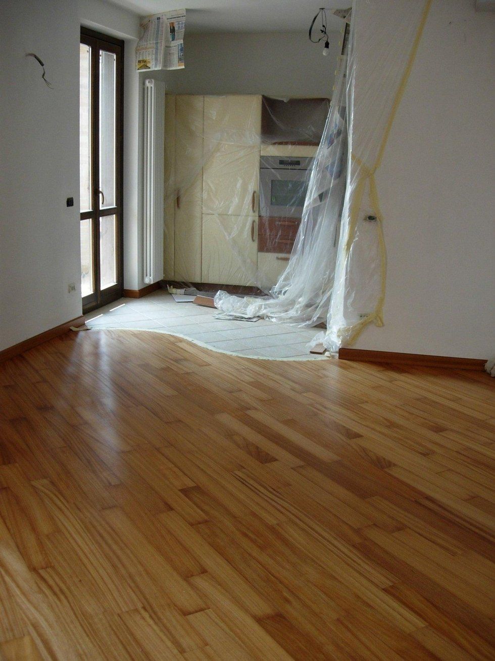 Pavimento in legno nella stanza con porta a sinistra. La zona cucina sullo sfondo è ricoperta di plastica durante la ristrutturazione.