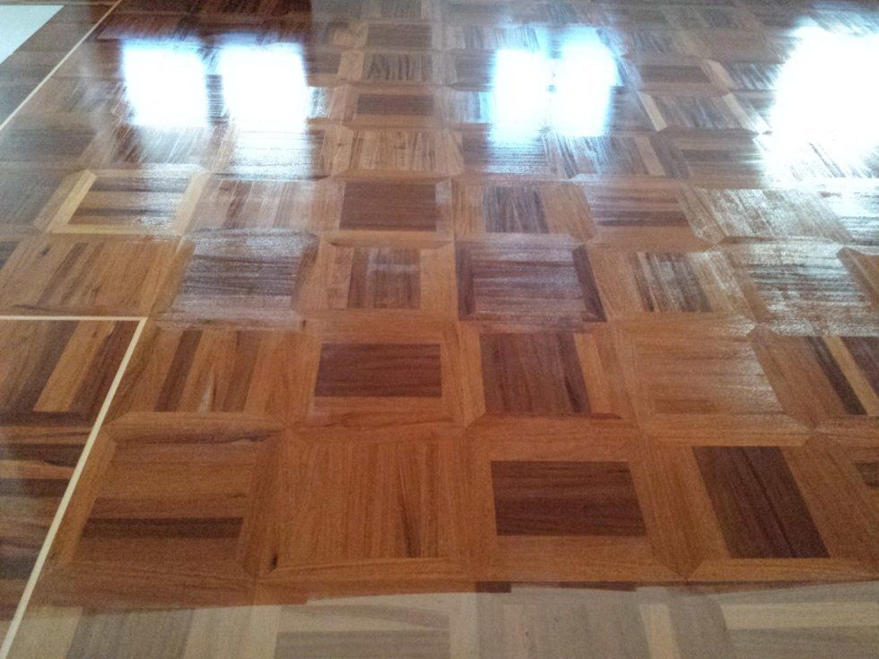 Pavimento in parquet di legno lucidato con motivo geometrico che riflette la luce proveniente dall'alto.