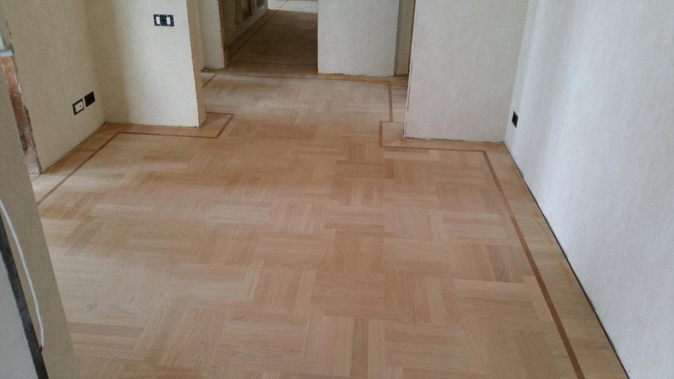 Pavimento in parquet con bordo scuro in una stanza dalle pareti chiare.
