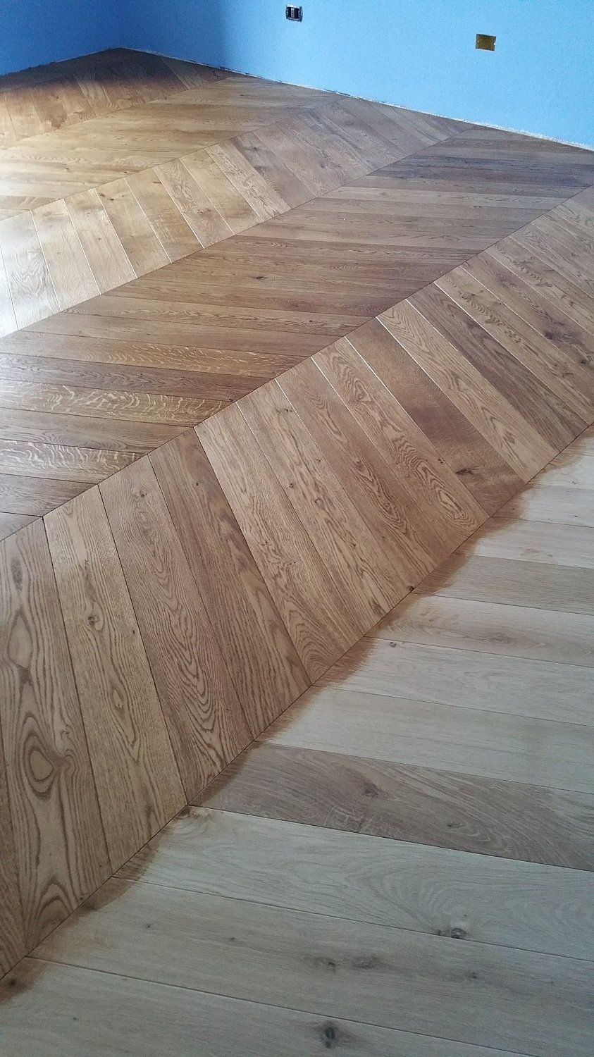Pavimento in legno con motivo a spina di pesce in diverse tonalità di marrone e beige.