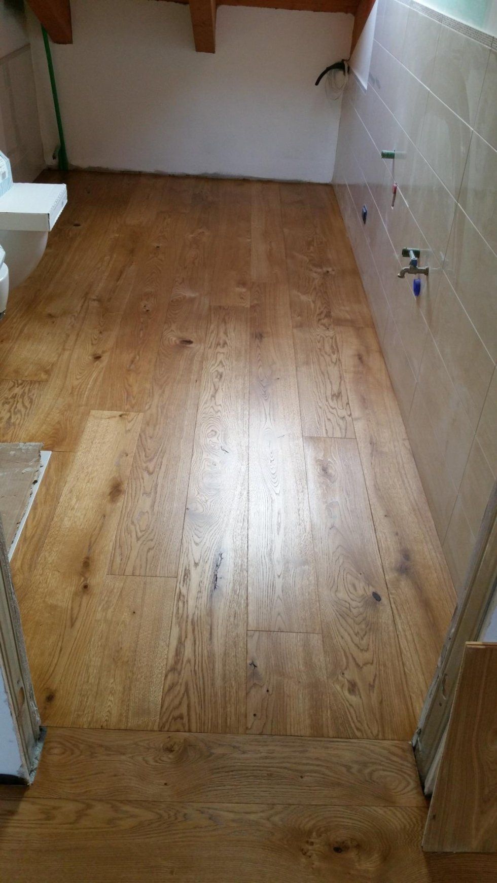 Pavimento in legno in un bagno con pareti e soffitto piastrellati, luce naturale.