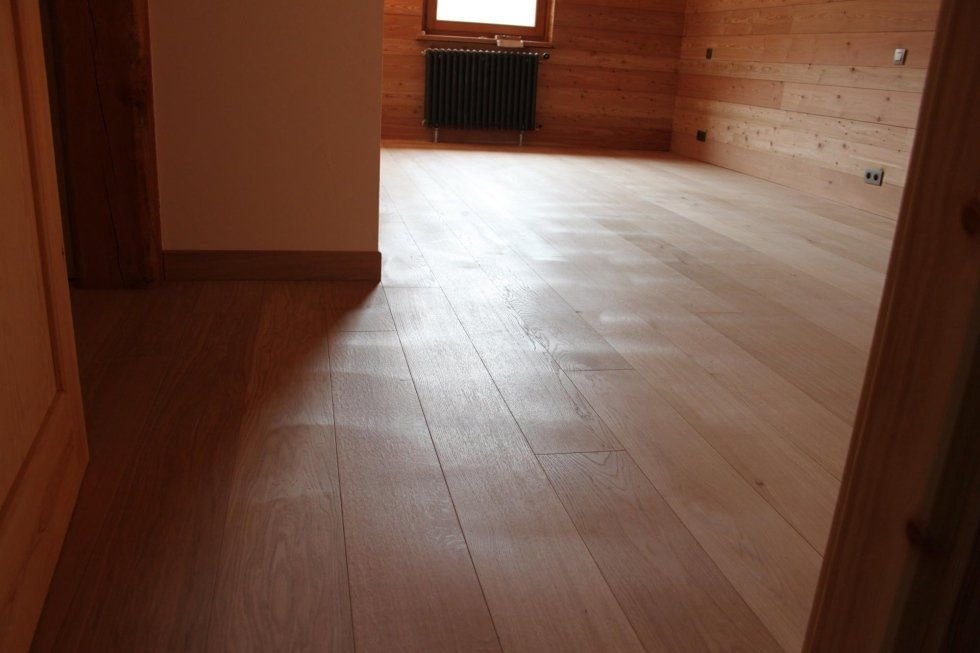 Pavimento in legno massello in una stanza con pareti in legno chiaro e un termosifone nero.