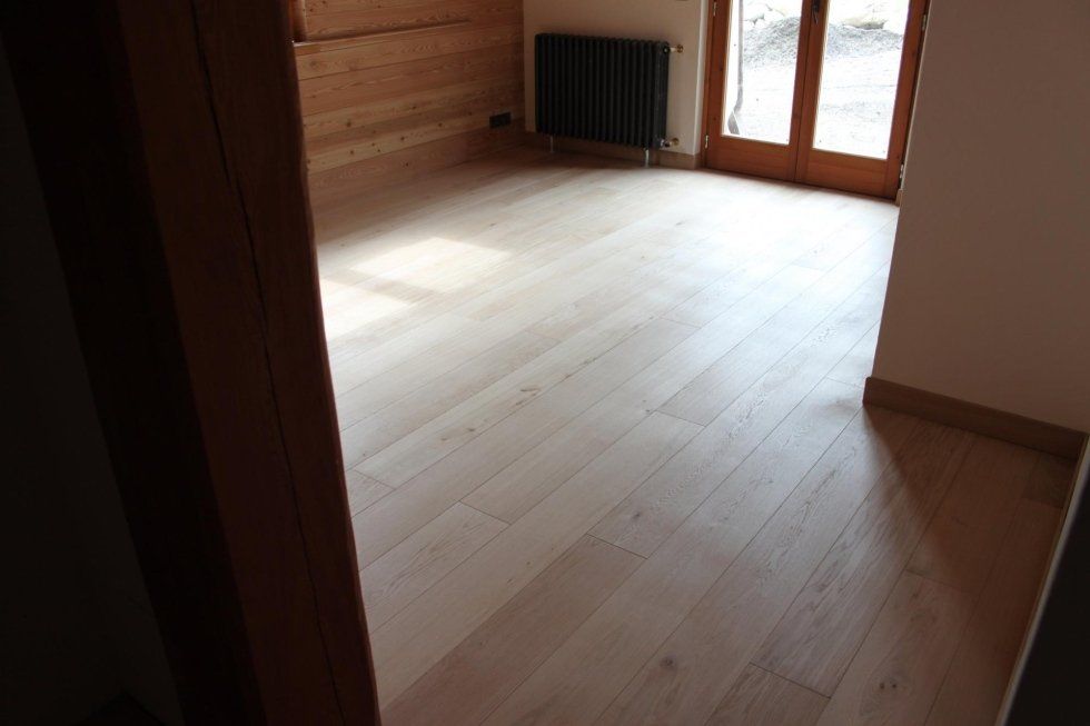 Stanza vuota con pavimenti in legno chiaro, pareti rivestite in legno, termosifone nero e porte in vetro.